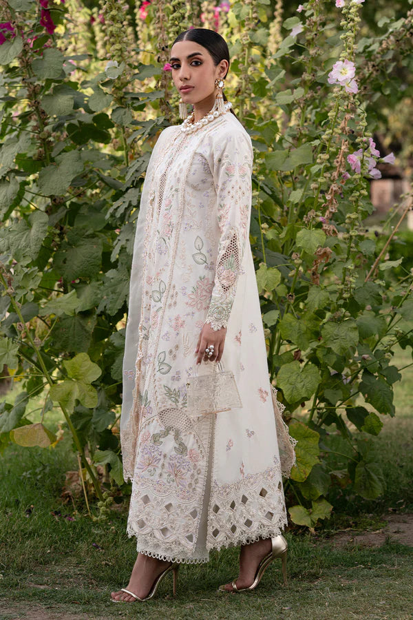 Woman in a white embroidered traditional outfit standing in a garden with greenery and flowers.