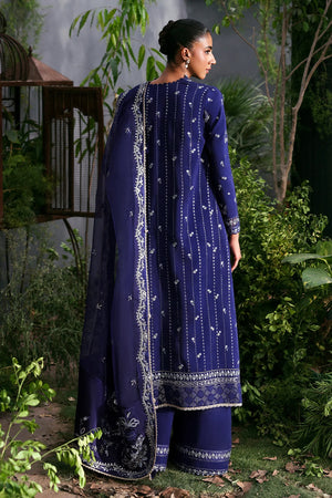 Woman wearing a traditional blue outfit with white patterns in a garden setting