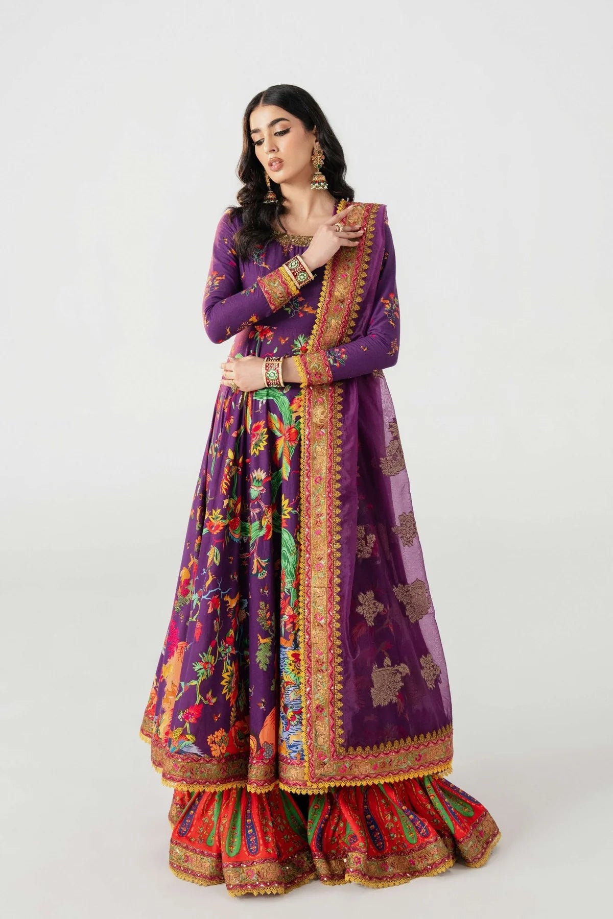 Woman wearing a colorful traditional outfit with a purple top and red skirt on a white background.
Mihrab By Ruuposh Collection 02