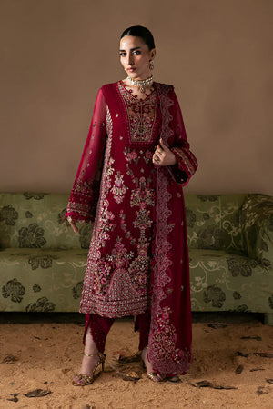 Woman in a red embroidered traditional outfit standing in front of a green sofa.