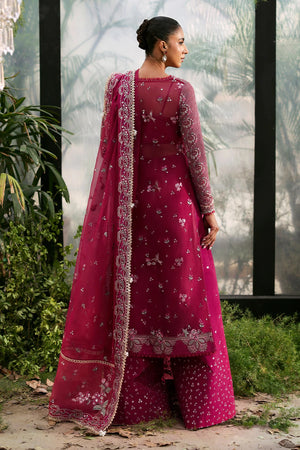 Rowan .Woman in a traditional pink embroidered outfit standing outdoors with greenery in the background