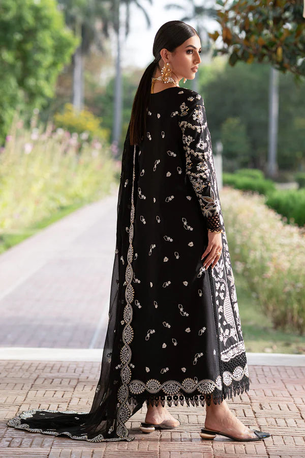 Woman in a black and white embroidered traditional outfit standing outdoors with greenery in the background