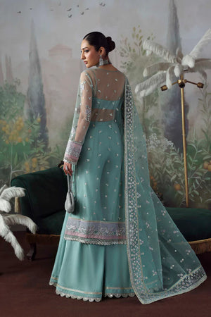 Woman in a teal traditional outfit with floral patterns in a decorative setting.