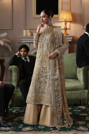 Woman in a traditional embroidered outfit standing in an elegant room with people and decor. Tajmeen