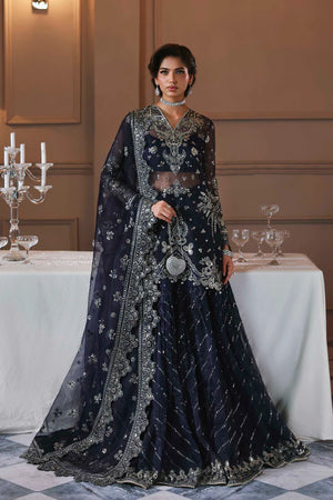 Zarpari. Woman in a dark blue embroidered traditional outfit standing in a formal setting with a table and candles.
